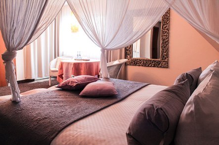 Ein elegantes Hotelzimmer mit Himmelbett, dekorativen Kissen und einem Tisch mit Stühlen. Ein großer Spiegel hängt an der Wand., © Hotel Princess