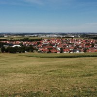 Grüne Wiesen führen zu einer Siedlung mit roten Dächern, umgeben von Feldern und Wäldern unter blauem Himmel., © Foto: Cornelia Steinbach
