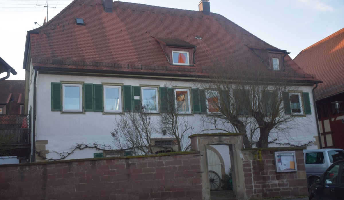 Ein zweistöckiges Gebäude mit rotem Ziegeldach und grünen Fensterläden hinter einer Steinmauer. Ein Torbogen führt in den Innenhof., © Land der 1000 Hügel - Kraichgau-Stromberg Ein zweistöckiges Gebäude mit rotem Ziegeldach und grünen Fensterläden hinter einer Steinmauer. Ein Torbogen führt in den Innenhof., © Land der 1000 Hügel - Kraichgau-Stromberg