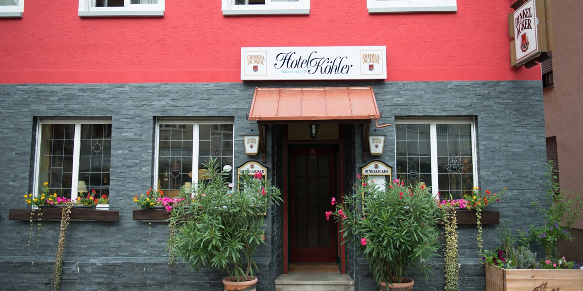 Das Hotel Köhler hat eine rote Fassade mit grauen Steinelementen. Vor dem Eingang stehen Pflanzen und bunte Blumen schmücken die Fenster., © Hotel Köhler Das Hotel Köhler hat eine rote Fassade mit grauen Steinelementen. Vor dem Eingang stehen Pflanzen und bunte Blumen schmücken die Fenster., © Hotel Köhler