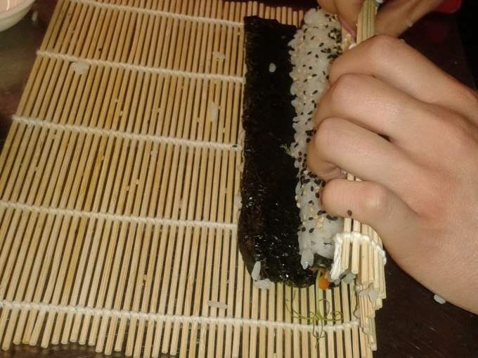Eine Person rollt Sushi mit einer Bambusmatte. Reis und Nori-Blatt sind sichtbar. H&auml;nde halten die Matte fest., &copy; Kultweine-Kochwelten-Kunst&uuml;cke - Kochschule Sonja Lenz