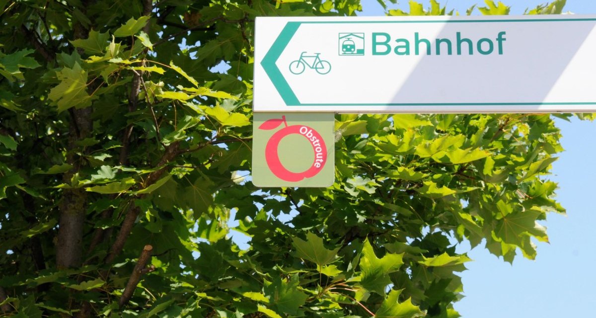 Ein Wegweiser zeigt zur Obstroute und zum Bahnhof, umgeben von grünen Blättern., © Baumgärtner Ein Wegweiser zeigt zur Obstroute und zum Bahnhof, umgeben von grünen Blättern., © Baumgärtner