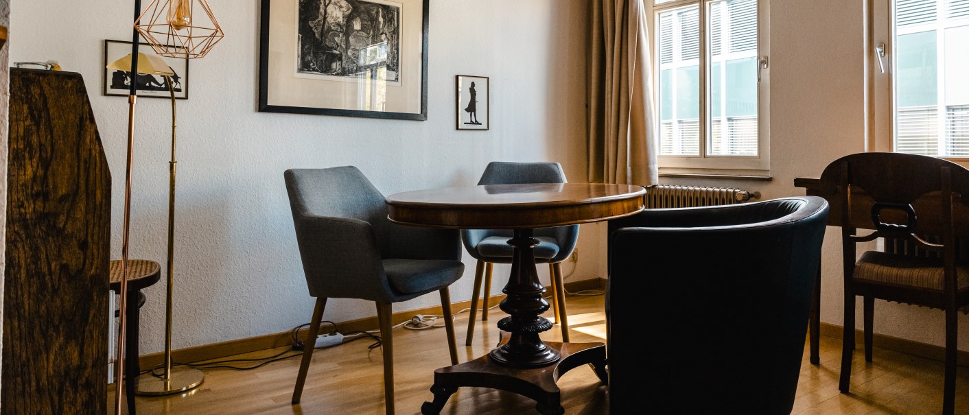 Ein gemütlicher Raum mit Holzbalken, einem runden Tisch, verschiedenen Stühlen und Kunstwerken an der Wand. Sonnenlicht fällt durch die Fenster., © SMG Stuttgart Marketing GmbH - Sarah Schmid Ein gemütlicher Raum mit Holzbalken, einem runden Tisch, verschiedenen Stühlen und Kunstwerken an der Wand. Sonnenlicht fällt durch die Fenster., © SMG Stuttgart Marketing GmbH - Sarah Schmid