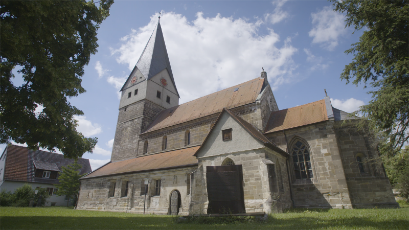 Die historische Kirche in Faurndau mit ihrem markanten spitzen Turm und roten Dachziegeln steht majest&auml;tisch unter einem klaren blauen Himmel.