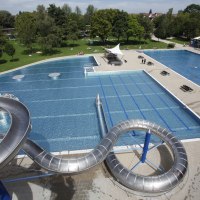 Freibad Rosental mit großer Wasserrutsche, mehreren Schwimmbecken und umliegenden Grünflächen. Menschen entspannen auf der Wiese., © Stuttgarter Bäder
