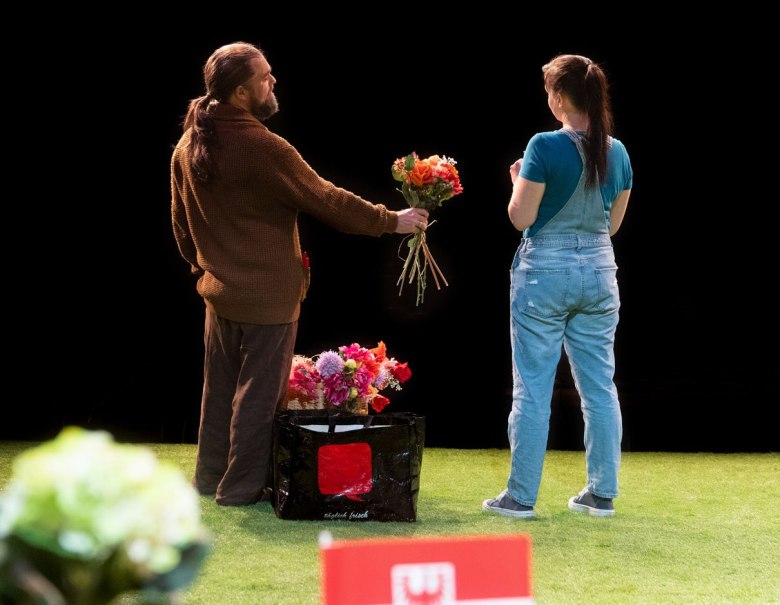 Zwei Personen stehen auf einer Bühne. Eine Person hält einen Blumenstrauß, während eine Tasche mit weiteren Blumen auf dem Boden steht., © Manuel Wagner Zwei Personen stehen auf einer Bühne. Eine Person hält einen Blumenstrauß, während eine Tasche mit weiteren Blumen auf dem Boden steht., © Manuel Wagner