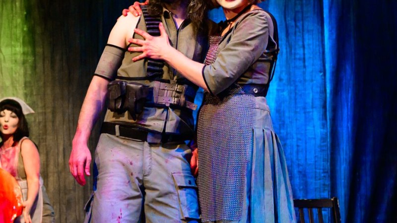 Zwei Schauspieler in auff&auml;lligen Kost&uuml;men und Gesichtsbemalung auf einer B&uuml;hne. Im Hintergrund spielt eine Musikerin Cello. Die Szene wirkt dramatisch., &copy; Ren&eacute; L&ouml;ffler