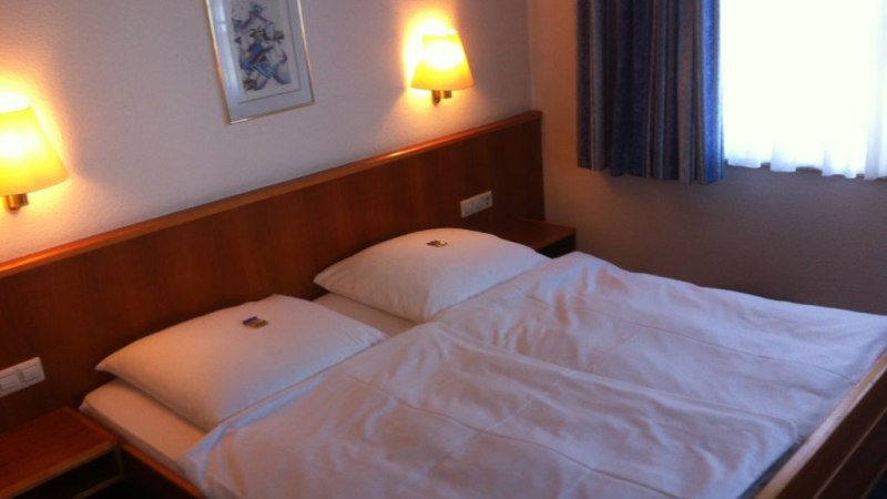 Ein gemütliches Doppelzimmer mit einem großen Bett, zwei Wandlampen und einem Bild an der Wand. Ein Fenster mit Vorhängen ist zu sehen., © Hotel Sonne garni Ein gemütliches Doppelzimmer mit einem großen Bett, zwei Wandlampen und einem Bild an der Wand. Ein Fenster mit Vorhängen ist zu sehen., © Hotel Sonne garni