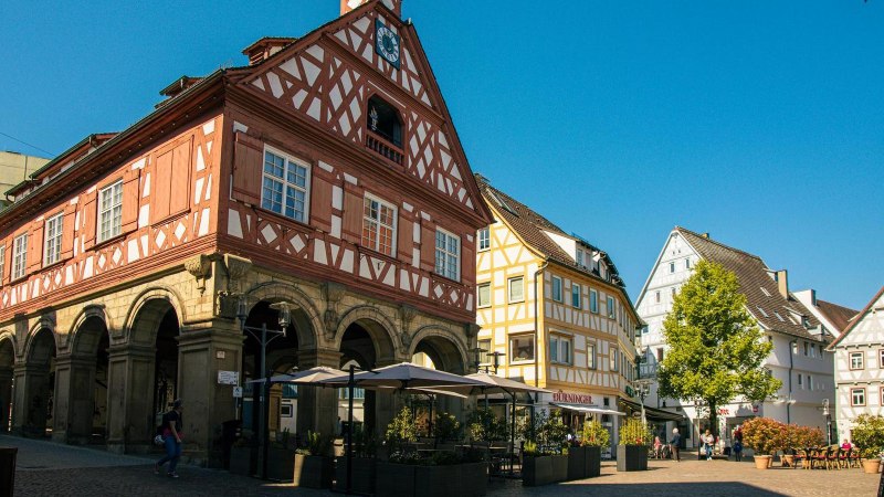 Historisches Fachwerkgebäude am Marktplatz in Waiblingen, umgeben von weiteren Fachwerkhäusern und einem Café im Freien bei sonnigem Wetter., © Stuttgart-Marketing GmbH, Sarah Schmid