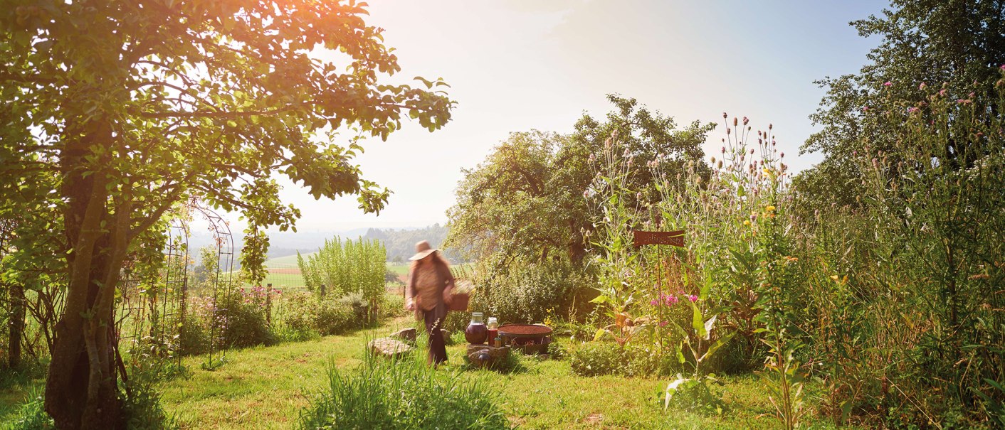 Eine Person mit Hut in einem sonnigen Garten mit Bäumen und hohen Pflanzen im Schwäbischen Wald., © Stuttgart-Marketing GmbH