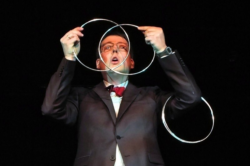 Ein Zauberer in Anzug und Fliege zeigt einen Trick mit ineinander verschlungenen Metallringen auf einer B&uuml;hne., &copy; LIMA-Theater