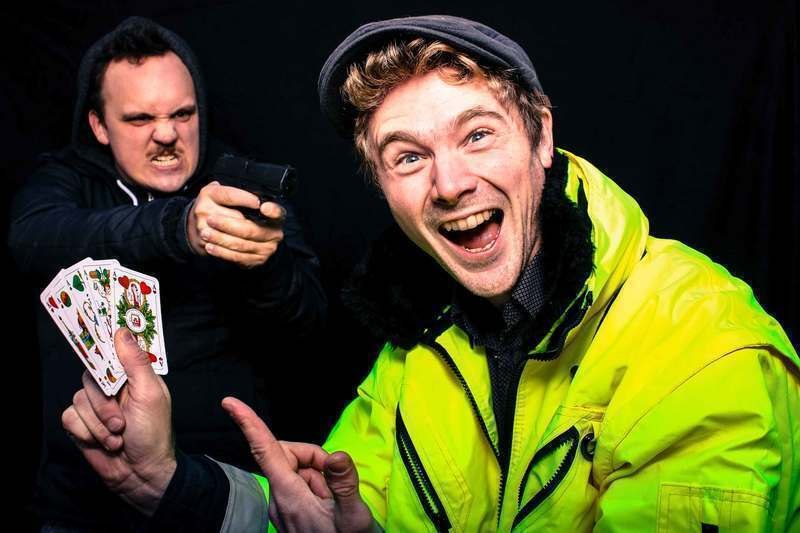 Ein Mann in gelber Jacke h&auml;lt lachend Spielkarten, w&auml;hrend ein anderer mit ernster Miene eine Spielzeugpistole auf ihn richtet., &copy; engesser marketing GmbH