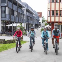 Vier Personen fahren mit Fahrrädern durch eine moderne Straße in Kirchheim unter Teck. Sie tragen Helme und Freizeitkleidung., © Schwäbische Alb Tourismusverband e.V.