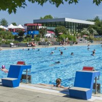 Ein Freibad mit vielen Schwimmern im Wasser. Im Hintergrund sind Liegestühle, Sonnenschirme und ein modernes Gebäude zu sehen., © Stadt Vaihingen an der Enz Ein Freibad mit vielen Schwimmern im Wasser. Im Hintergrund sind Liegestühle, Sonnenschirme und ein modernes Gebäude zu sehen., © Stadt Vaihingen an der Enz