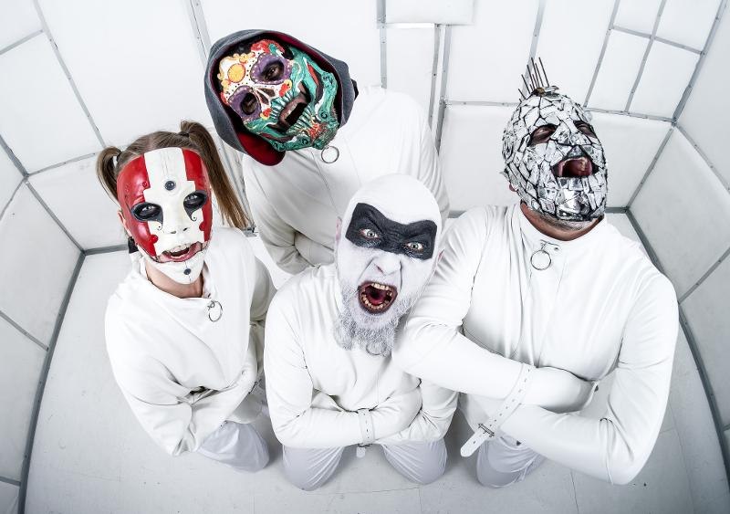 Vier Personen tragen weiße Zwangsjacken und bunte Masken in einem weißen, gepolsterten Raum. Sie schauen zur Kamera und haben die Arme verschränkt., © Music Circus Concertbüro GmbH & Co. KG