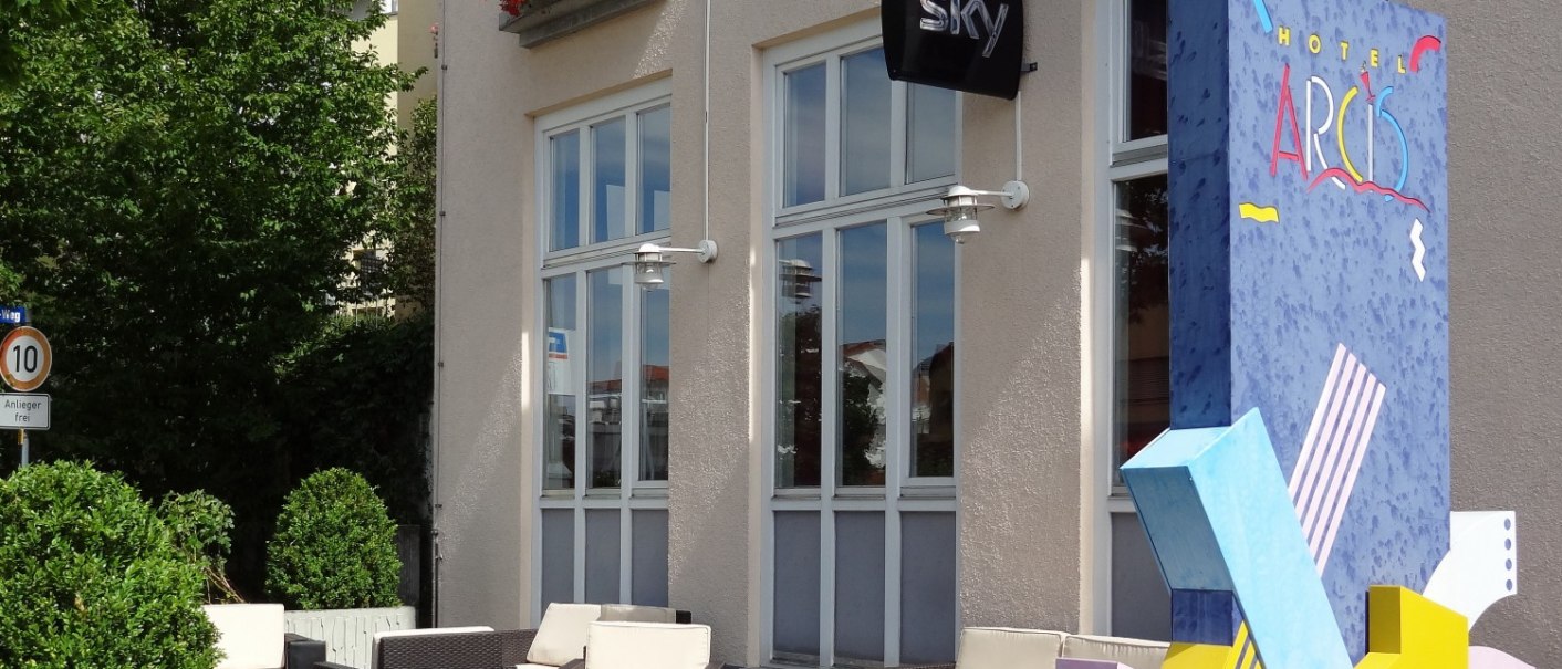 Terrasse des Hotels Arcis mit Sitzmöbeln und bunter Dekoration. Schilder für Brasserie und Sky sind sichtbar. Blumen schmücken die Fenster., © Hotel Arcis Terrasse des Hotels Arcis mit Sitzmöbeln und bunter Dekoration. Schilder für Brasserie und Sky sind sichtbar. Blumen schmücken die Fenster., © Hotel Arcis