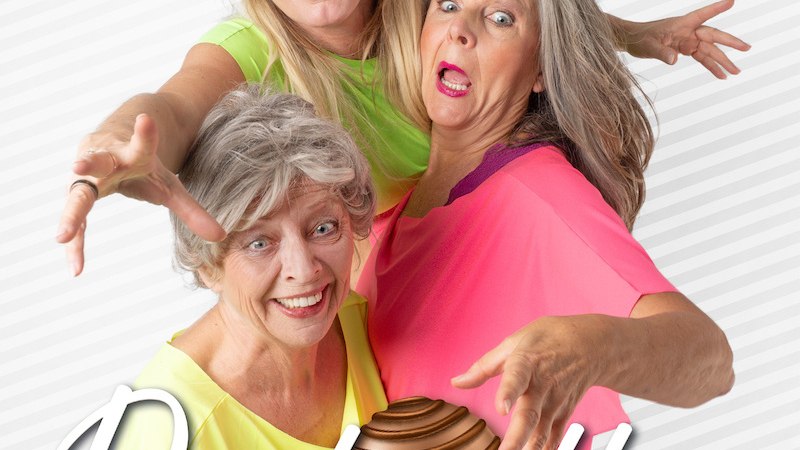 Drei fr&ouml;hliche Frauen in bunten Oberteilen posieren mit einer gro&szlig;en Praline vor einem gestreiften Hintergrund. Der Schriftzug 'Pralin&eacute;tten' ist zu sehen., &copy; Agentur Siedepunkt