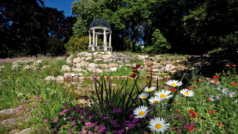Ein bl&uuml;hender Garten mit bunten Blumen, einem kleinen Teich und einem Pavillon im Hintergrund, umgeben von B&auml;umen., &copy; Staatsministerium Baden-W&uuml;rttemberg