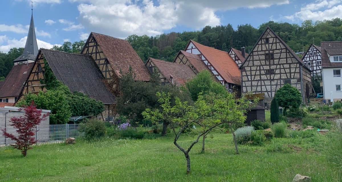Fachwerkhäuser mit roten Dächern und ein Kirchturm in einem Dorf, umgeben von grüner Landschaft und Bäumen., © Land der 1000 Hügel - Kraichgau-Stromberg Fachwerkhäuser mit roten Dächern und ein Kirchturm in einem Dorf, umgeben von grüner Landschaft und Bäumen., © Land der 1000 Hügel - Kraichgau-Stromberg