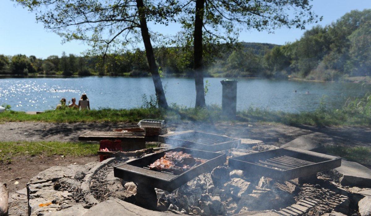 Grillstelle mit Fleisch am Seeufer, im Hintergrund Menschen am Wasser. Bäume und blauer Himmel umrahmen die Szene., © Land der 1000 Hügel - Kraichgau-Stromberg Grillstelle mit Fleisch am Seeufer, im Hintergrund Menschen am Wasser. Bäume und blauer Himmel umrahmen die Szene., © Land der 1000 Hügel - Kraichgau-Stromberg