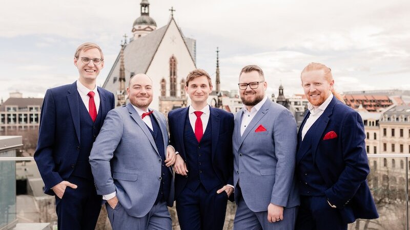 Fünf Männer in eleganten Anzügen stehen auf einer Terrasse. Im Hintergrund ist eine Kirche zu sehen. Sie lächeln in die Kamera., © Kammerkonzerte Schwäbisch Hall e.V.