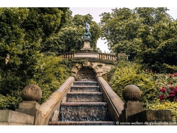 Steintreppe mit Wasserfall, flankiert von Bäumen und Sträuchern, führt zu einer Statue auf einer Balustrade., © Stuttgart Marketing GmbH Steintreppe mit Wasserfall, flankiert von Bäumen und Sträuchern, führt zu einer Statue auf einer Balustrade., © Stuttgart Marketing GmbH