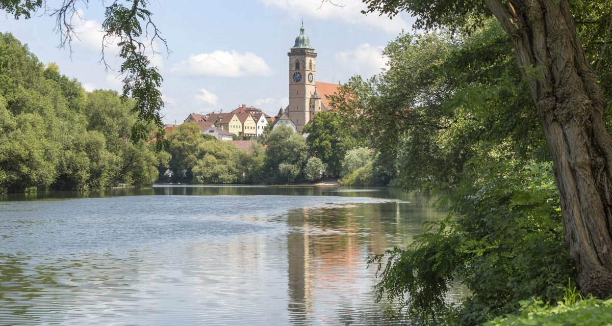 Blick auf Nürtingen mit einer Kirche im Hintergrund, umgeben von Bäumen. Ein ruhiger Fluss fließt im Vordergrund, umrahmt von grüner Vegetation., © Stadt Nürtingen, D. Jüptner Blick auf Nürtingen mit einer Kirche im Hintergrund, umgeben von Bäumen. Ein ruhiger Fluss fließt im Vordergrund, umrahmt von grüner Vegetation., © Stadt Nürtingen, D. Jüptner