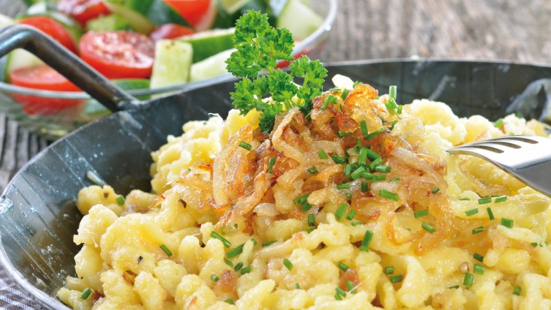 K&auml;sesp&auml;tzle mit R&ouml;stzwiebeln und Schnittlauch in einer Pfanne, daneben ein frischer Salat mit Tomaten und Gurken., &copy; kab-vision - Fotolia