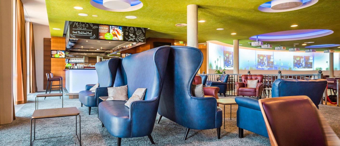Moderne Hotelbar mit blauen Sesseln, grüner Decke und beleuchteter Theke. Gemütliche Atmosphäre mit stilvollen Möbeln und Dekoration., © Hilton Garden Inn Stuttgart Neckarpark Moderne Hotelbar mit blauen Sesseln, grüner Decke und beleuchteter Theke. Gemütliche Atmosphäre mit stilvollen Möbeln und Dekoration., © Hilton Garden Inn Stuttgart Neckarpark