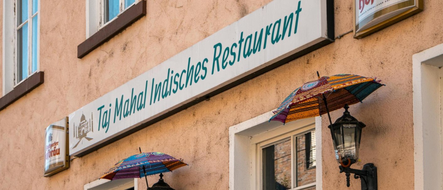 Fassade eines indischen Restaurants in Stuttgart mit bunten Schirmen und einem Schild mit der Aufschrift 'Taj Mahal Indisches Restaurant'., © SMG, Sarah Schmid
